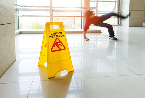 Man slips falling on wet floor next to the wet floor caution sign.